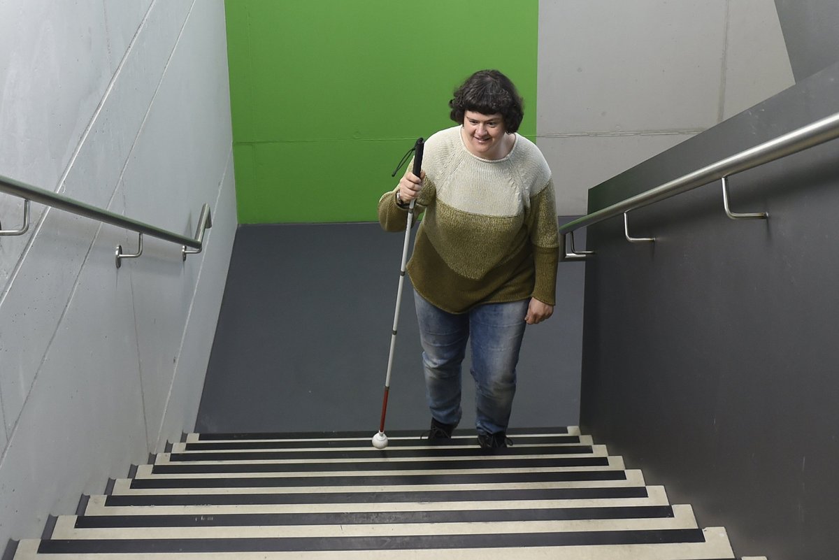Eine Frau läuft mithilfe eines weißen Langstockes die Treppe nach oben